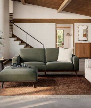 Green mid-century modern sofa with matching ottoman in a living room with a wood beam ceiling.