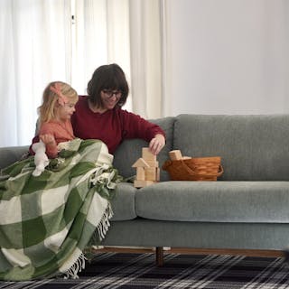 A green fabric sofa with walnut legs styled with a family and child in a living room.