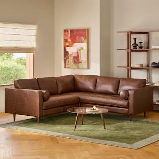 Chocolate brown leather Sven corner sectional sofa with tufted seats and bolster pillows, styled with a glass coffee table and green rug.