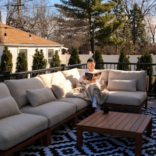 Person reading on the Cove 102.75" Outdoor Armless Modular Sectional in Basket Beige. Photo by @nomukaugc