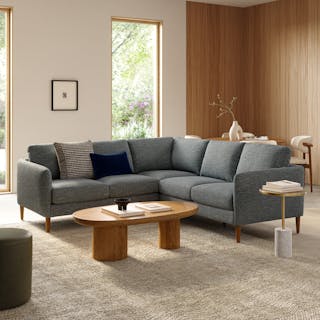 A dark gray fabric corner sectional with walnut legs in a bright modern living room.