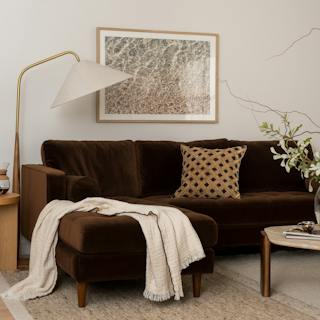 Brown velvet Sven sectional sofa with a chaise, cream throw blanket, and patterned accent pillow in a cozy living room.