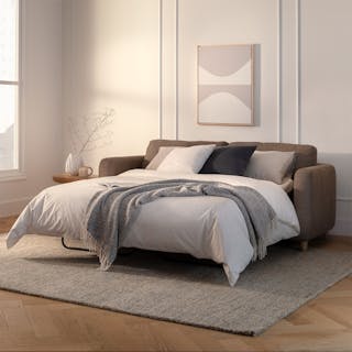 A brown sofa bed opened into a bed with white bedding in a bright, minimal living room.
