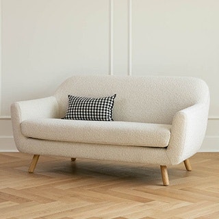 An ivory-colored bouclé loveseat with a patterned pillow on a wooden floor.