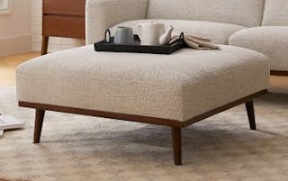Ivory ottoman with walnut legs in front of a matching sofa, styled with a serving tray.