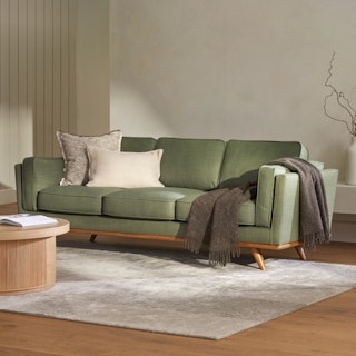 A green sofa with pillows and a throw in a bright living room.