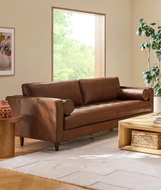 Sven sofa in Taos Brown leather with a tufted bench seat and bolster pillows in a sunlit organic modern living room.