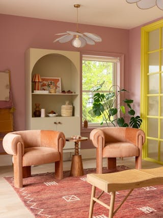 Stylish living room with pink walls, plush armchairs, and warm wood accents.