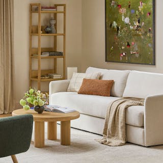 An ivory fabric sofa bed in a living room with a round wood coffee table and bookshelf styled around it.