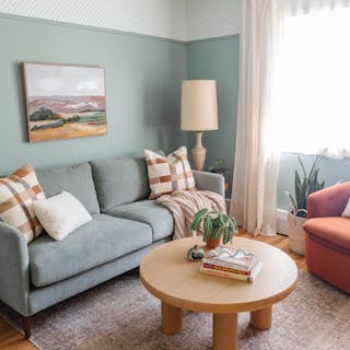 A green fabric sofa with walnut legs in a living room with a round wood coffee table.